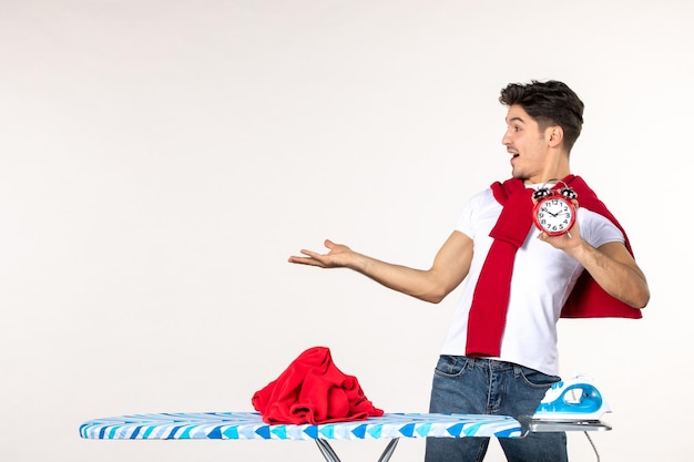 Front view young male behind ironing board holding clocks on white background man laundry home housework clean emotions time color work