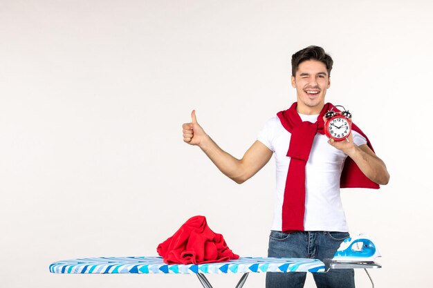 Front view young male behind ironing board holding clocks on white