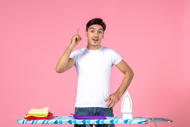 Front view young male behind ironing board on pink background work clean effort emotion man clothes home