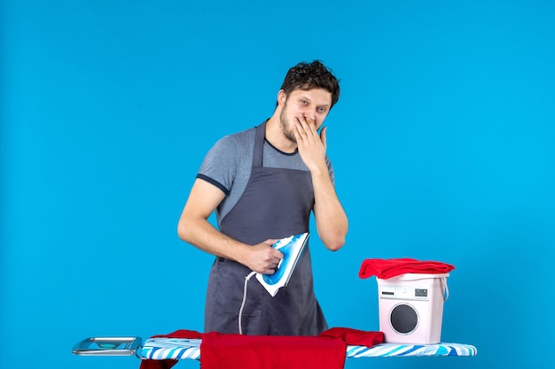 Front view young male ironing red shirt on blue surface