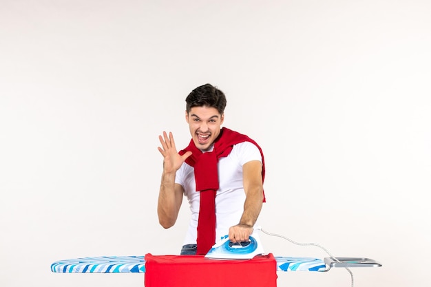 Вид спереди молодой мужчина гладит красное полотенце на белом фоне мужчина работа по дому эмоция дома чистая работа цвет стирки