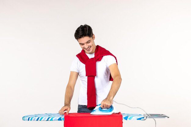 Vista frontale giovane maschio che stira asciugamano rosso su sfondo bianco uomo lavori domestici emozione casa pulito lavoro lavanderia colore