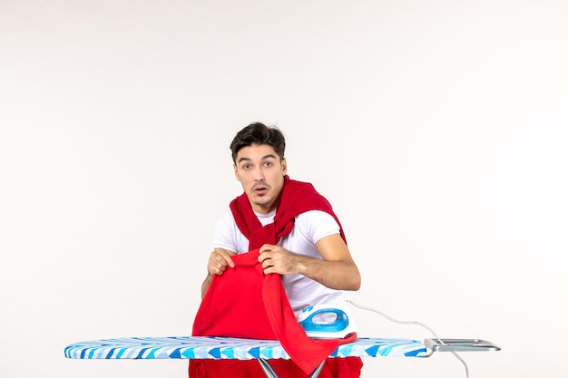 Front view young male ironing towel on a white surface