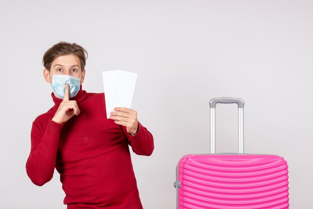 Front view of young male in mask holding tickets on the white wall