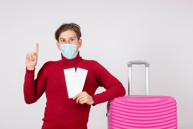 Front view of young male in mask holding tickets on the white wall