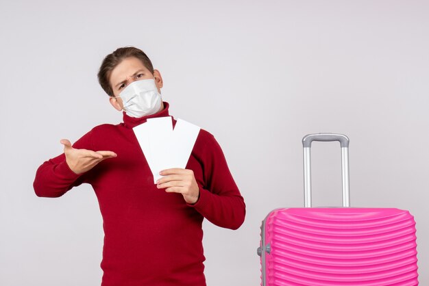 Front view of young male in mask holding tickets on white wall