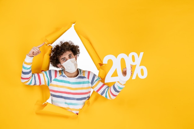 Front view young male in mask holding writing on yellow coronavirus health covid- sale color photo