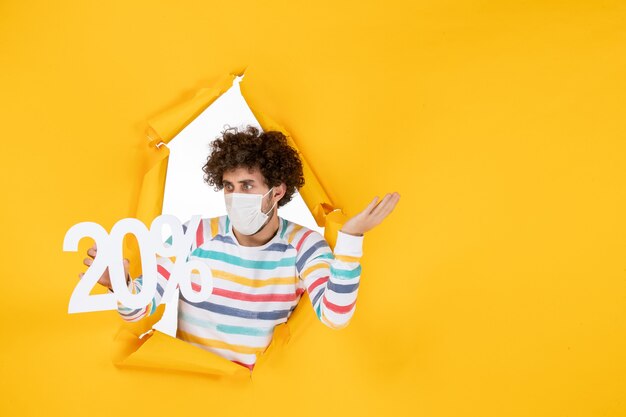 Вид спереди молодой мужчина в маске держит письмо на желтом пандемическом здоровье коронавируса - распродажа цветные фотографии