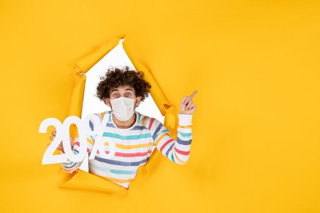 Front view young male in mask holding writing on a yellow coronavirus pandemic photo health covid- sale color