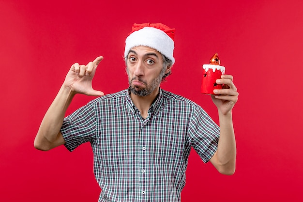 Front view of young male measuring size of little toy on red