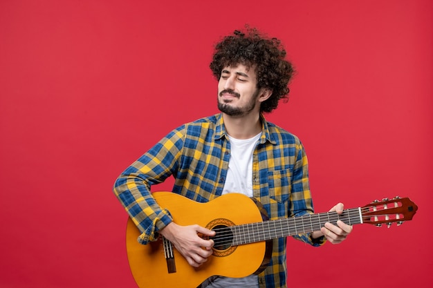 Front view young male playing guitar on red wall concert live play color band applause music musician