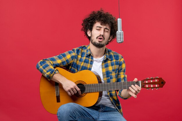 正面図ギターを弾き、赤い壁のバンド歌手のライブパフォーマンスミュージシャンコンサートカラーで歌う若い男性