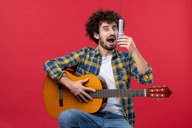 전면 보기 젊은 남성 기타 연주와 붉은 벽 밴드 가수 공연 음악가 콘서트 컬러 음악에 노래