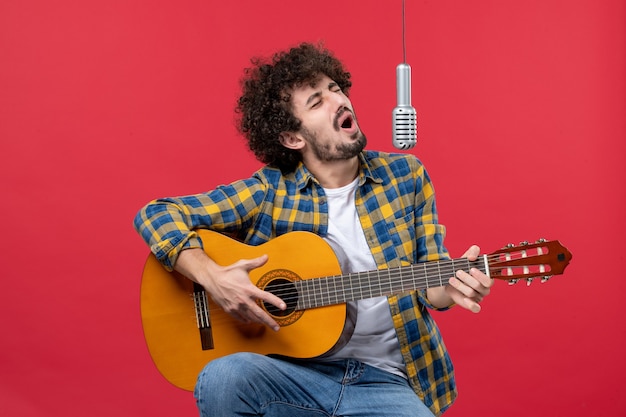 Front view young male playing guitar and singing on a red wall band singer performance musician concert live color