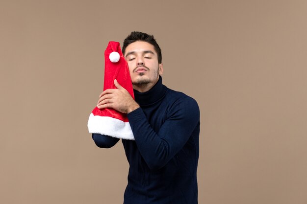 Front view young male playing with red cap on a brown background christmas emotion new year