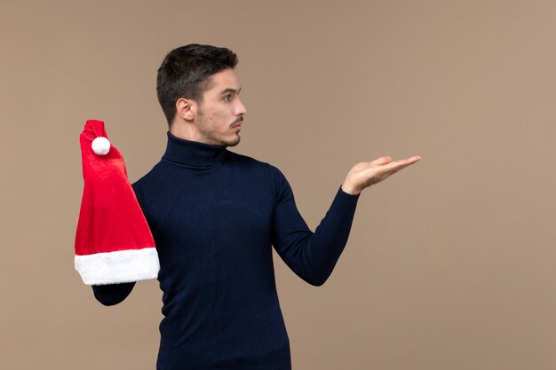 Front view young male playing with red cap on a brown background christmas emotions holiday