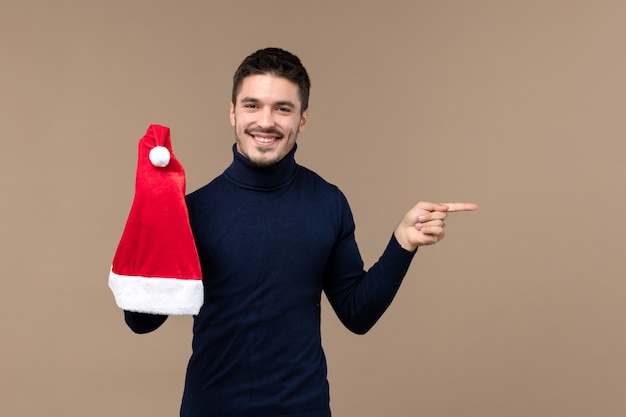 Front view young male playing with red cap on a brown background emotion christmas new year