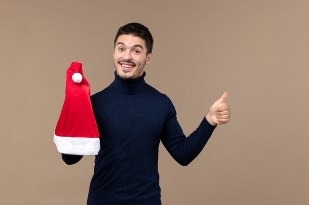 Giovane maschio di vista frontale che gioca con il cappuccio rosso su sfondo marrone emozioni natale capodanno