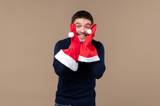 Foto gratuita giovane maschio di vista frontale che gioca con i cappucci rossi sull'emozione marrone di festa di natale dello scrittorio