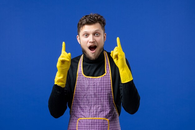 Front view of young male pointing at ceiling standing on blue wall