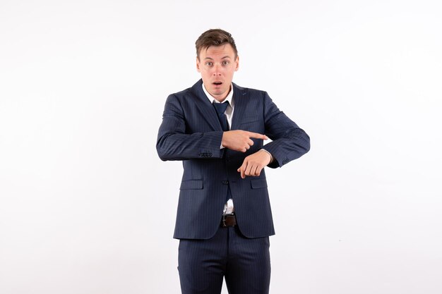 Front view young male pointing at his wrist in classic strict suit on white background