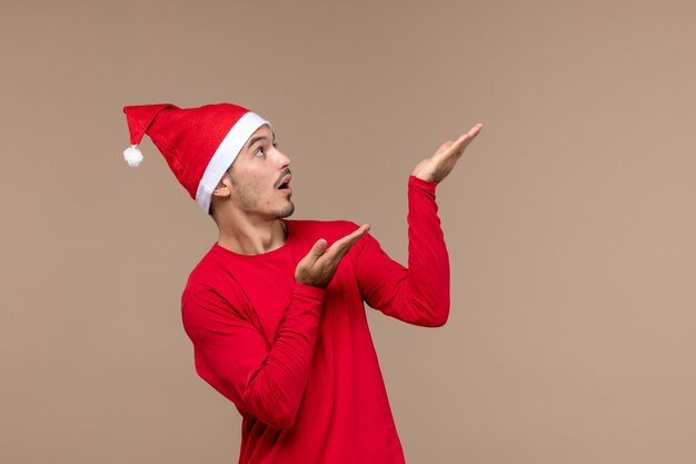 Вид спереди молодой мужчина позирует с удивленным лицом на коричневом фоне эмоции праздник рождество