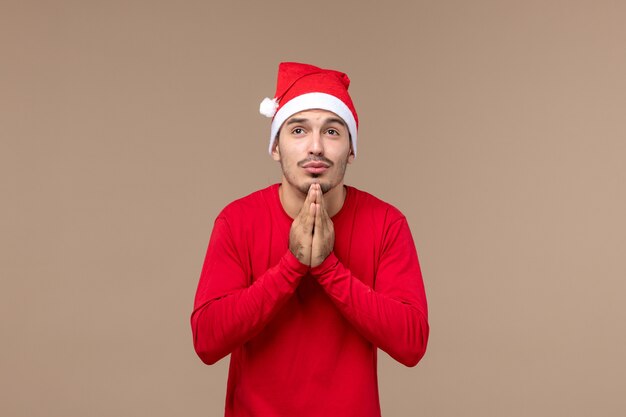 Вид спереди молодой мужчина молится на коричневом фоне рождественские эмоции праздник