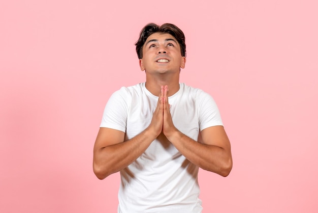 ピンクの背景に白いTシャツで祈る正面図若い男性
