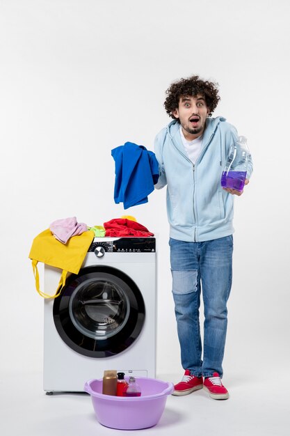 Front view of young male preparing dirty clothes for washer on a white wall