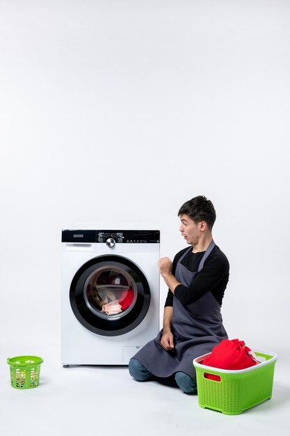 Front view of young male preparing dirty clothes for washer on the white wall