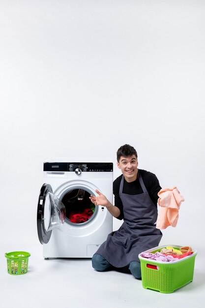 Front view of young male preparing dirty clothes for washing on white wall