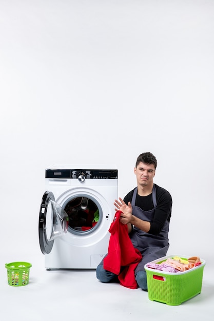 Front view of young male preparing dirty clothes for washing on white wall