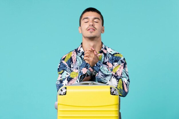 Front view of young male preparing for trip with his yellow bag on blue wall