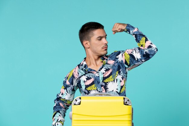 Front view of young male preparing for trip with his yellow bag and flexing on blue wall