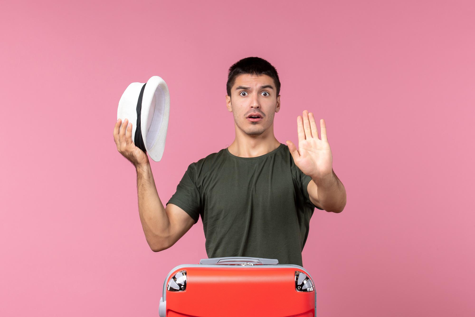 Front view young male preparing for vacation holding hat on light pink space