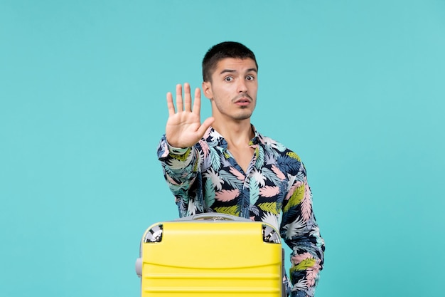 Front view of young male preparing for vacation and showing stop sign on blue wall