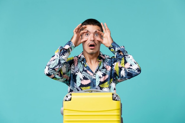 Front view of young male preparing for vacation with bag posing on light-blue wall