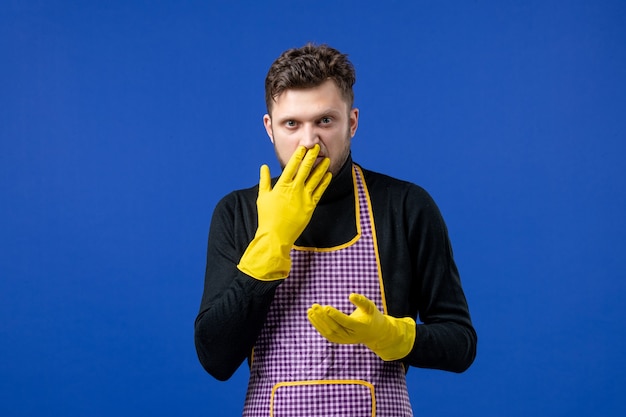Front view of young male putting hand in front of his nose standing on blue wall