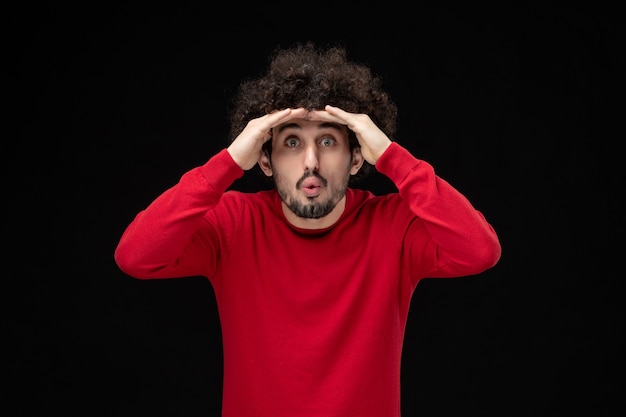 Front view of young male in red shirt on black wall