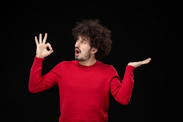 Front view of young male in red shirt on black wall