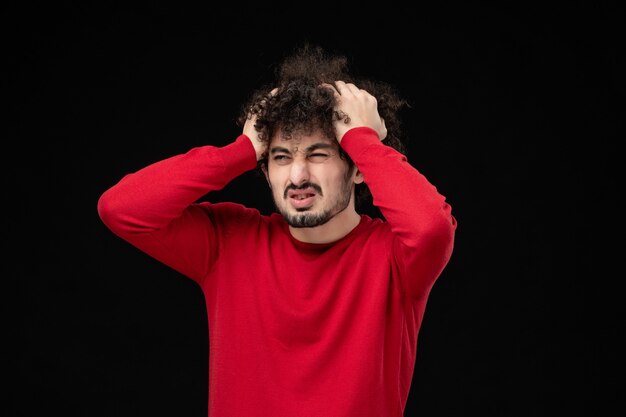 Front view of young male in red shirt on black wall