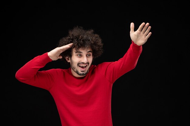 Front view of young male in red shirt on a black wall