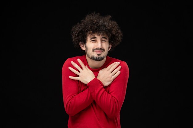 Front view of young male in red shirt on a black wall