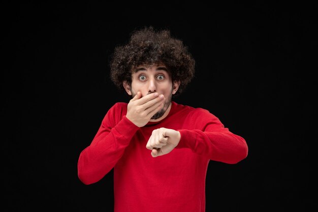 Front view of young male in red shirt checking time on a black wall