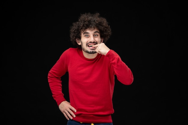 Вид спереди молодого мужчины в красной рубашке, возбужденного на черной стене