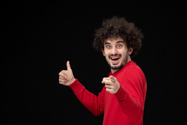 Front view of young male in red shirt feeling excited on black wall