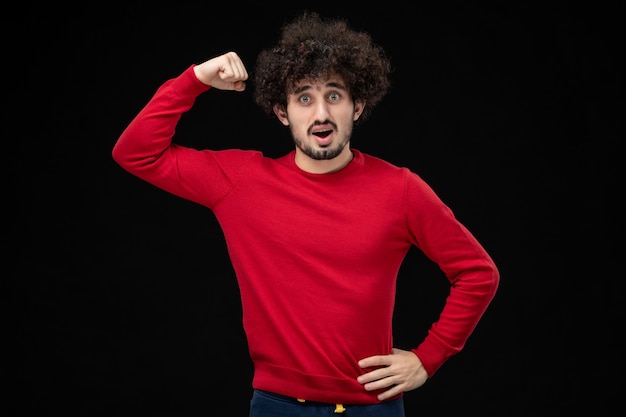 Front view of young male in red shirt flexing on black wall
