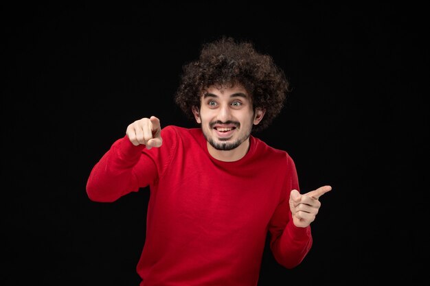 Front view of young male in red sweater on black wall