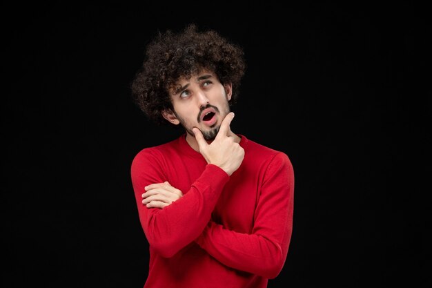 Front view of young male in red sweater on black wall