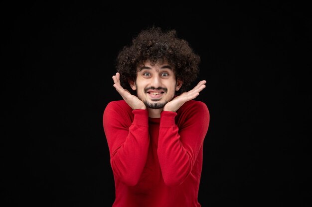 Front view of young male in red sweater on black wall